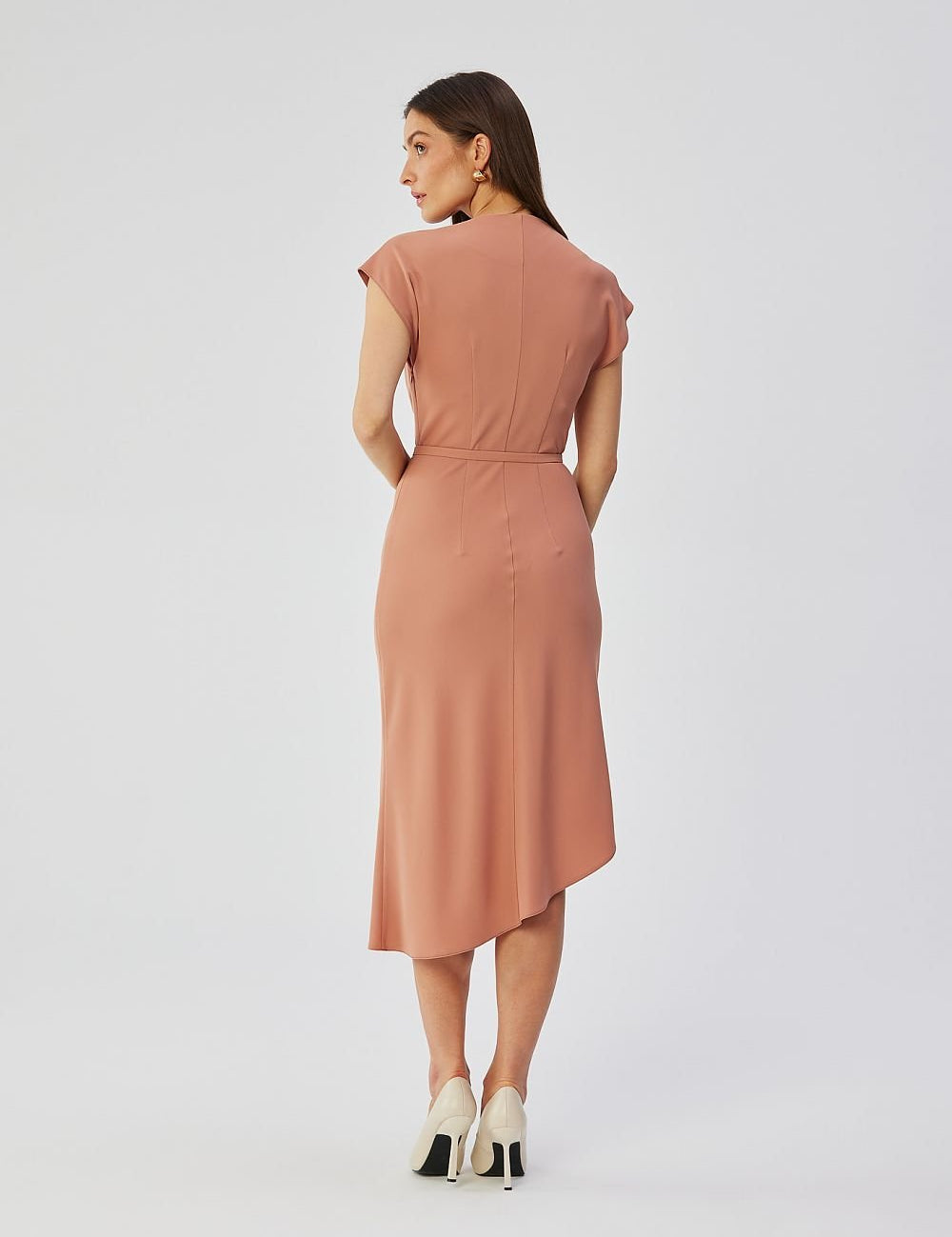 Back view of a woman wearing a Calerra Asymmetric Midi Pencil Dress in pink, featuring a slanted hem and matching belt for waist definition.