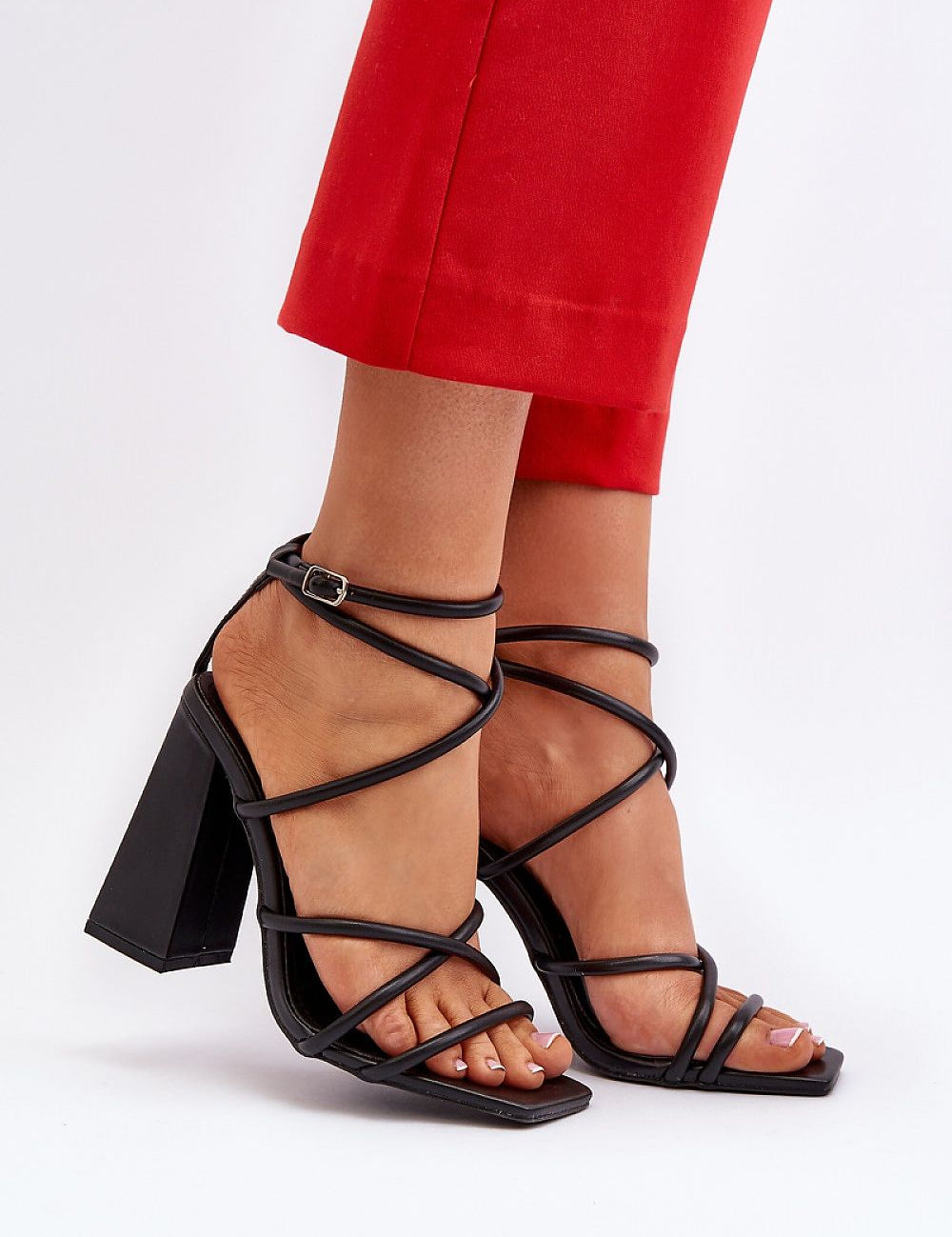 Model wearing Eliore High Heel Buckled Sandals with eco leather straps and wide post heel in a minimalist design, paired with red pants.