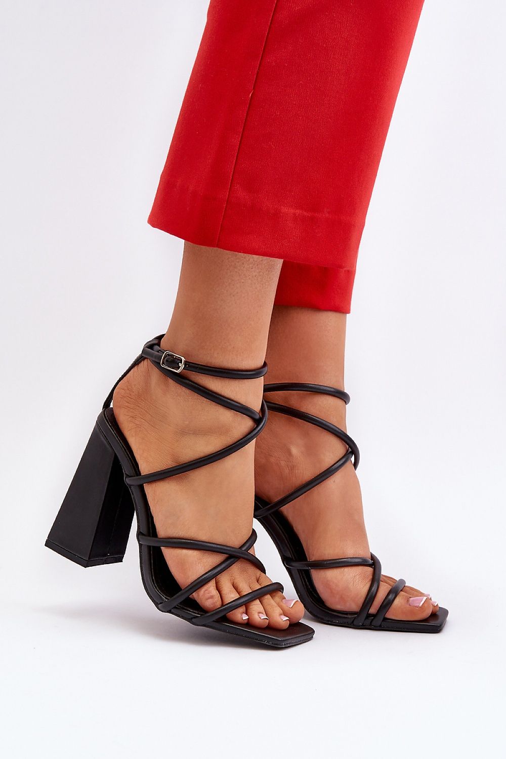Model wearing Eliore High Heel Buckled Sandals with eco leather straps and wide post heel in a minimalist design, paired with red pants.