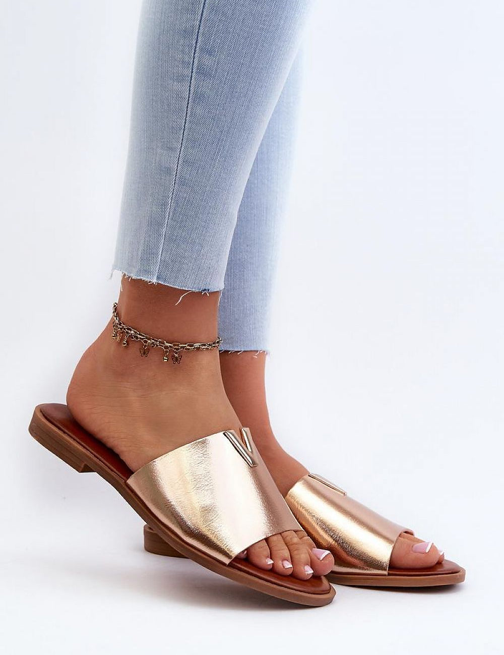 Talvera flat slides in gold on person wearing jeans, featuring eco leather and slim heel, perfect for summer fashion.