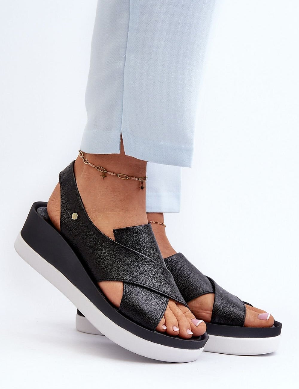 Woman wearing Buskin Model 198813 black leather slip-on sandals with platform and elegant emblem design.