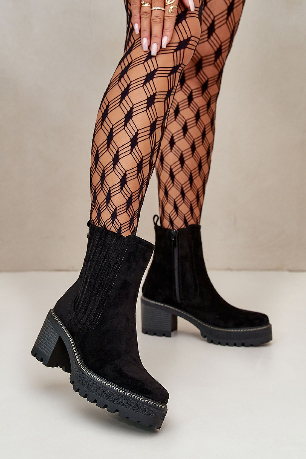 Woman wearing black suede-finish ankle boots with block heel and patterned tights, showcasing stylish footwear in a modern setting.