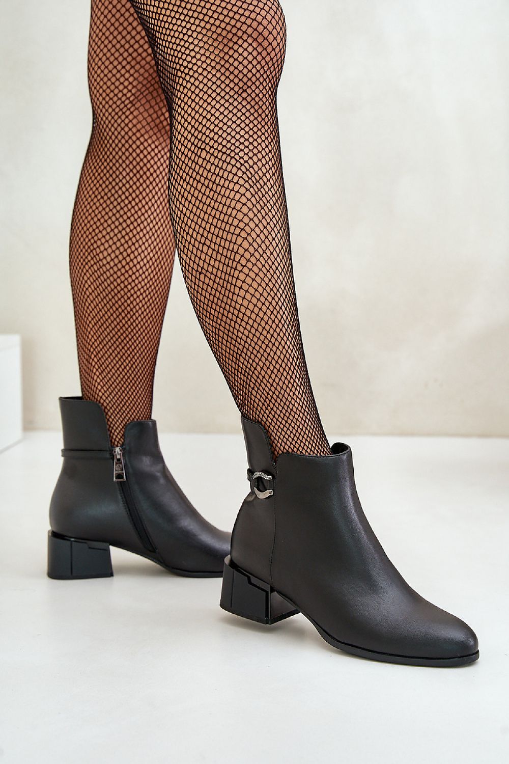 Woman wearing Malvory sleek high-heel ankle boots with decorative strap and side zipper, showcasing elegance and structure in black leather.