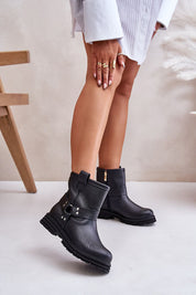 Woman wears black leather ankle boots with side zipper and buckle, showcasing elegant design on smooth white floor background.