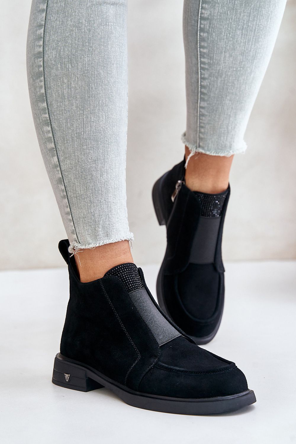 Person wearing Lunavea suede ankle boots with zip and decorative tongue detail, showing side zipper and rounded toe, on light background.