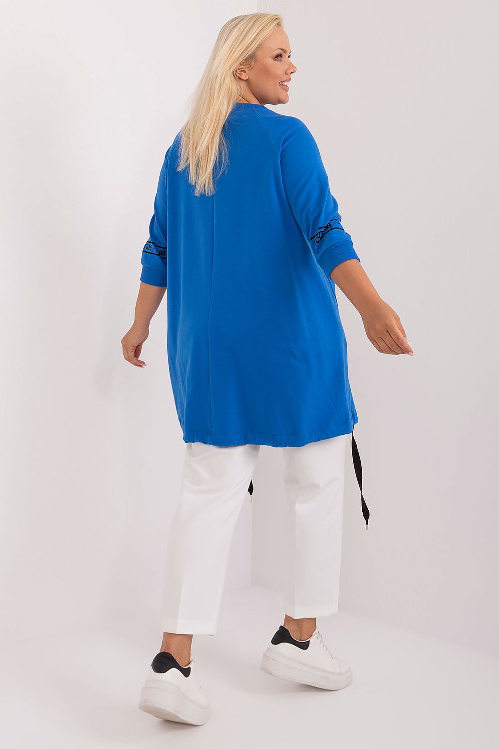 Back view of woman in blue Elverra Plus Size Rhinestone Blouse with asymmetrical cut and 3/4 sleeves, paired with white pants.