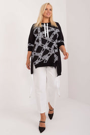 Plus size model wearing Elverra rhinestone blouse with asymmetric cut and 3/4 sleeves, paired with white pants.