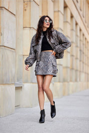 Woman wearing Vionera cropped suede-effect jacket with animal pattern, black top, matching skirt, and black boots walking on city street.