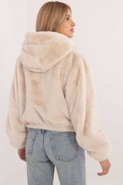 Woman wearing cream faux fur hooded jacket paired with blue jeans, viewed from the back.