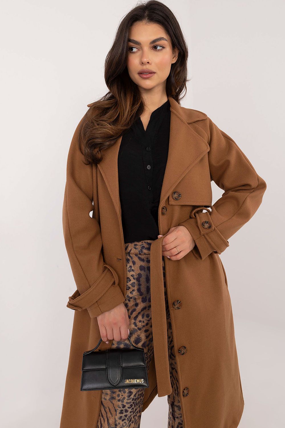 Woman wearing Meriselle Belted Weather-Resistant Trench in brown, featuring button closure and waist belt, paired with leopard print pants.