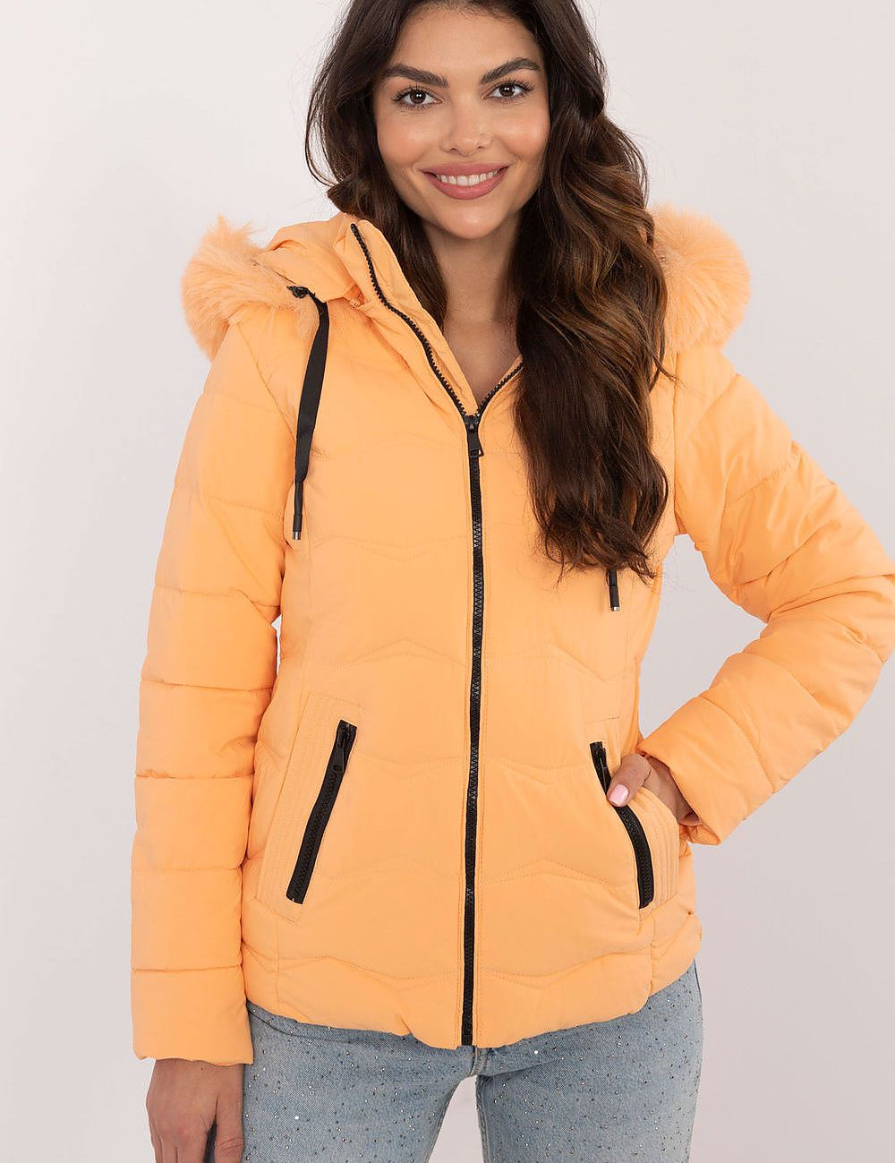 Woman wearing Veyra Short Quilted Jacket in orange with detachable hood and front zipper, showcasing sleek winter fashion.
