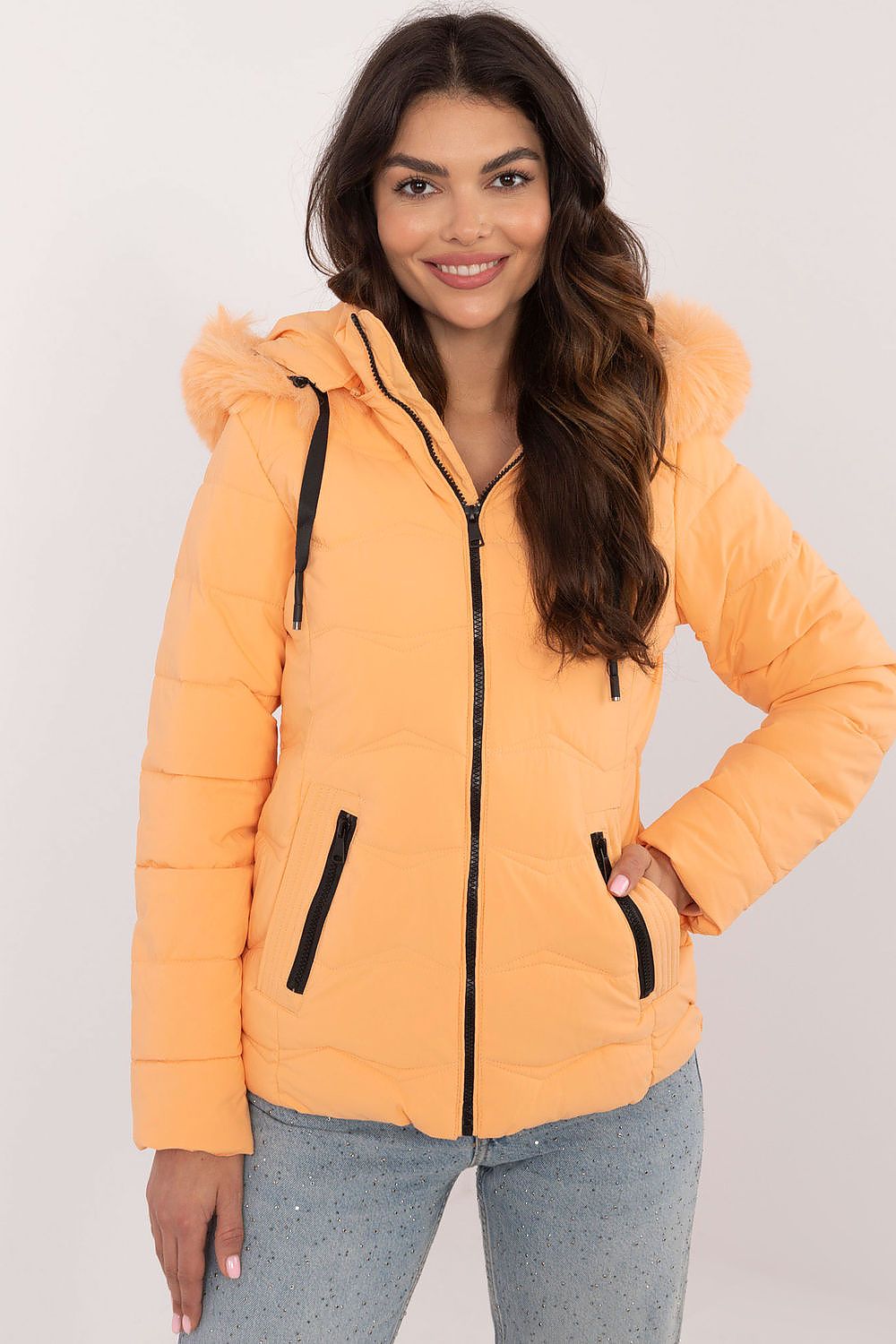 Woman wearing Veyra Short Quilted Jacket in orange with detachable hood and front zipper, showcasing sleek winter fashion.