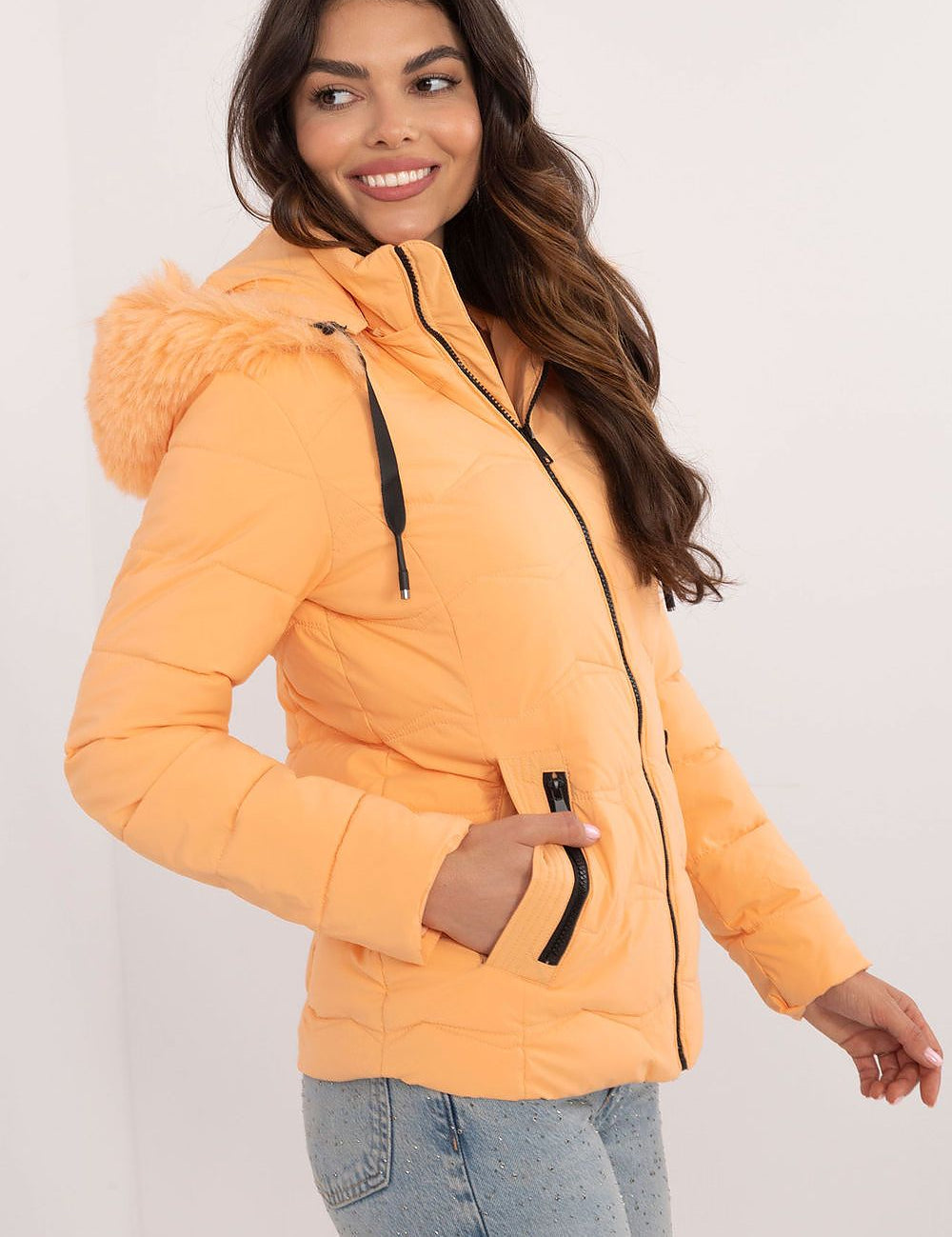 Woman wearing Veyra Short Quilted Jacket in orange with detachable hood, showcasing sleek and warm cold-weather style.