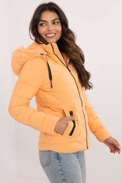 Woman wearing Veyra Short Quilted Jacket in orange with detachable hood, showcasing sleek and warm cold-weather style.