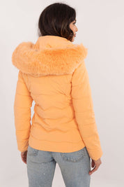 Woman wearing Veyra Short Quilted Jacket in orange with detachable hood and fur trim, back view showing quilted design.
