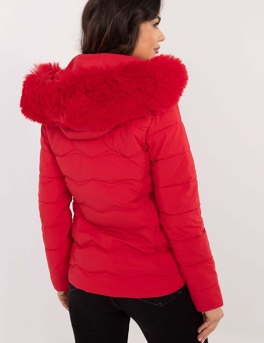 Woman wearing a red Veyra Short Quilted Jacket with a detachable hood, showcasing its sleek design and quilted pattern from the back view.