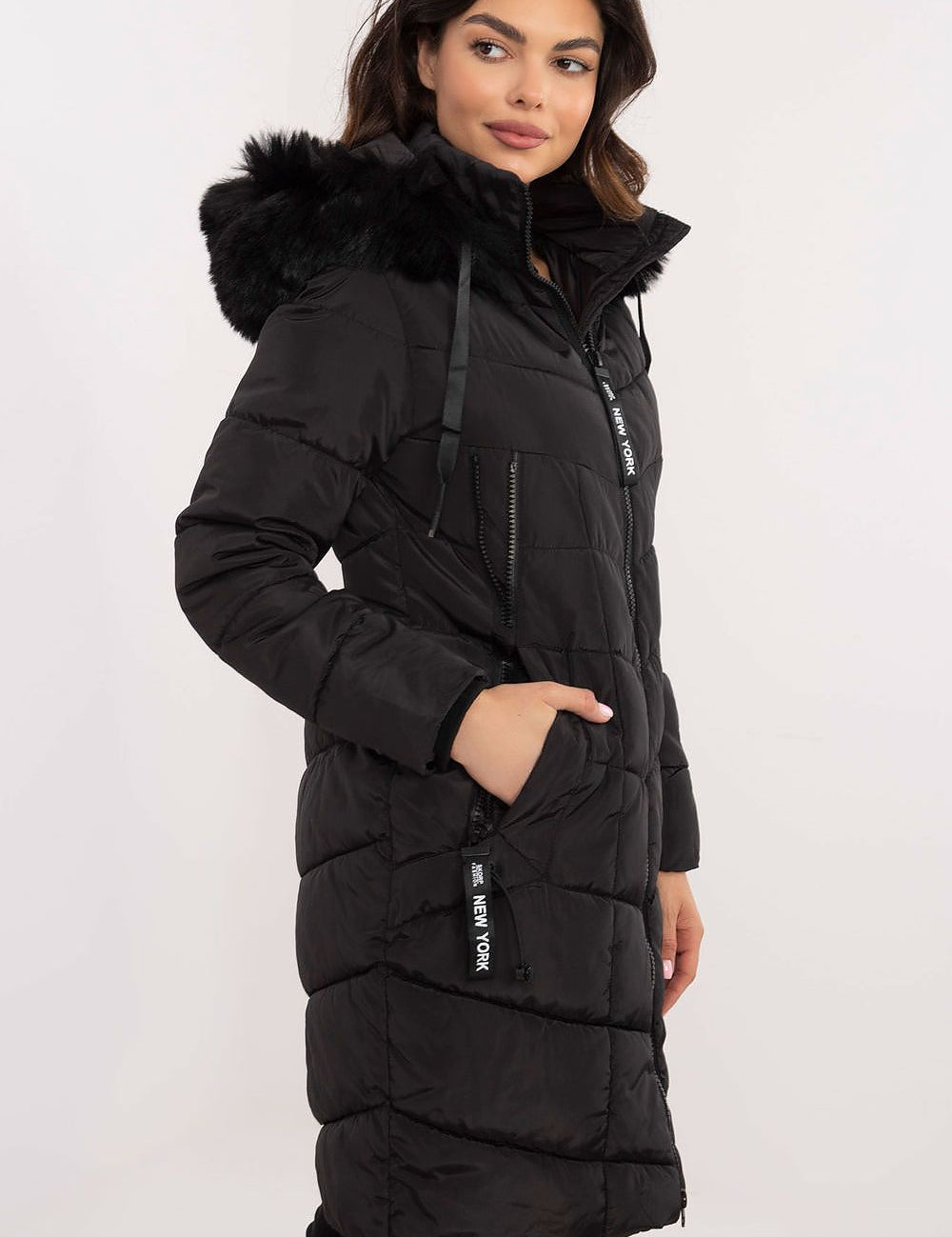 Woman wearing Aurlis Quilted Winter Jacket with detachable faux fur trim, side view, black color, knee-length, warm and stylish design.