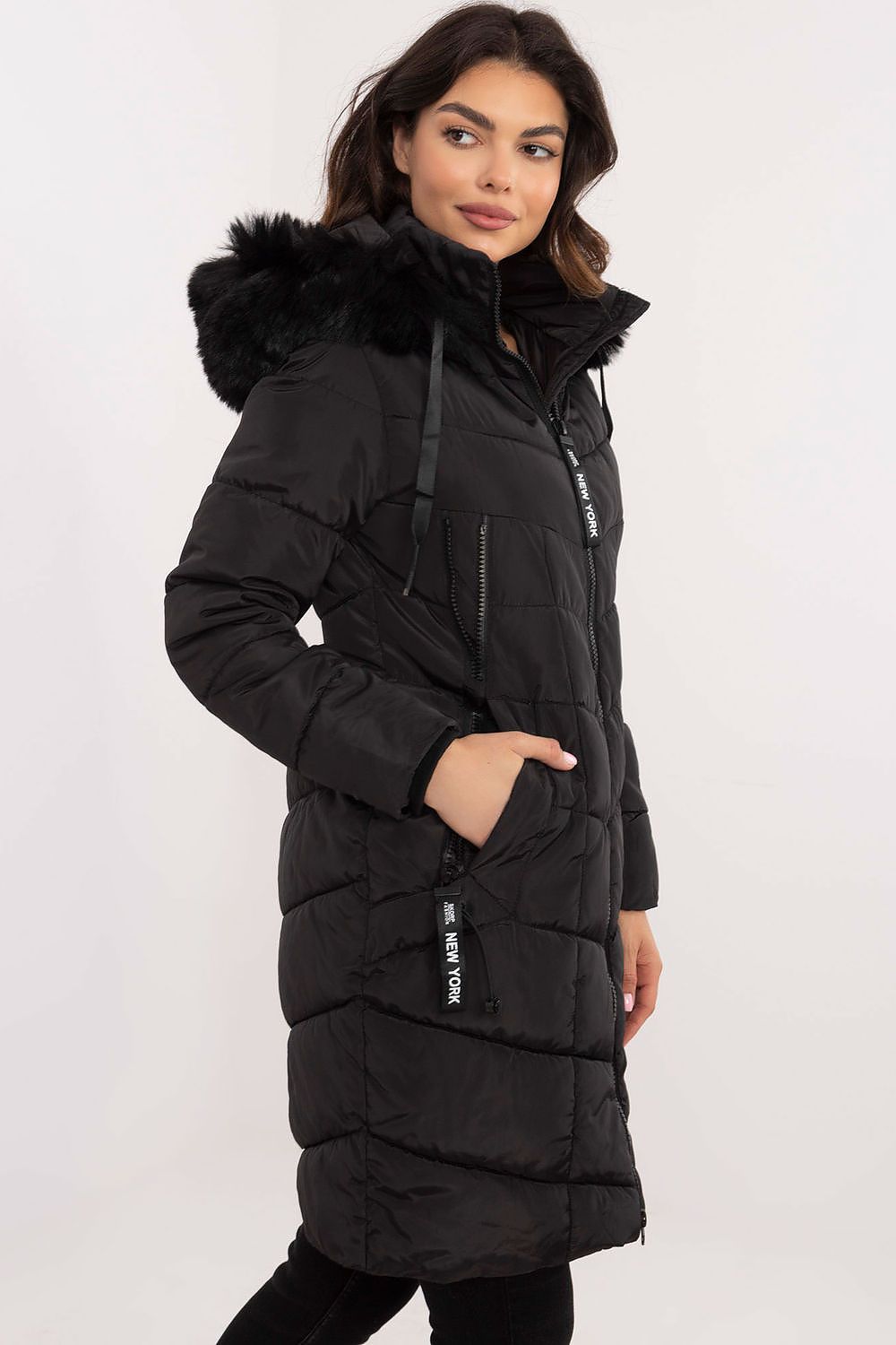 Woman wearing Aurlis Quilted Winter Jacket with detachable faux fur trim, side view, black color, knee-length, warm and stylish design.