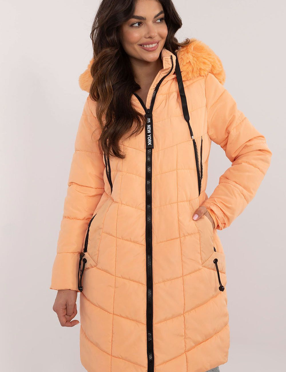 Woman wearing Aurlis Quilted Winter Jacket, peach, with detachable faux fur trim, knee-length coverage for warmth and style.