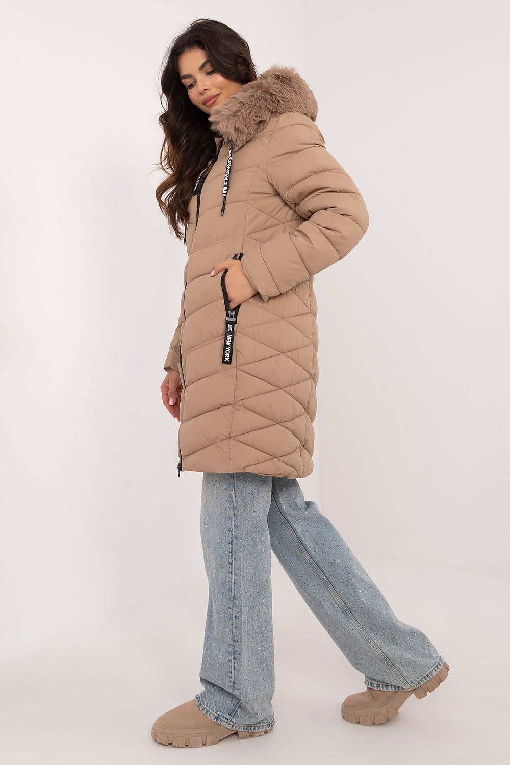 Woman wearing a knee-length Frostveil Quilted Winter Jacket with detachable faux fur hood and stylish quilted design, paired with jeans.
