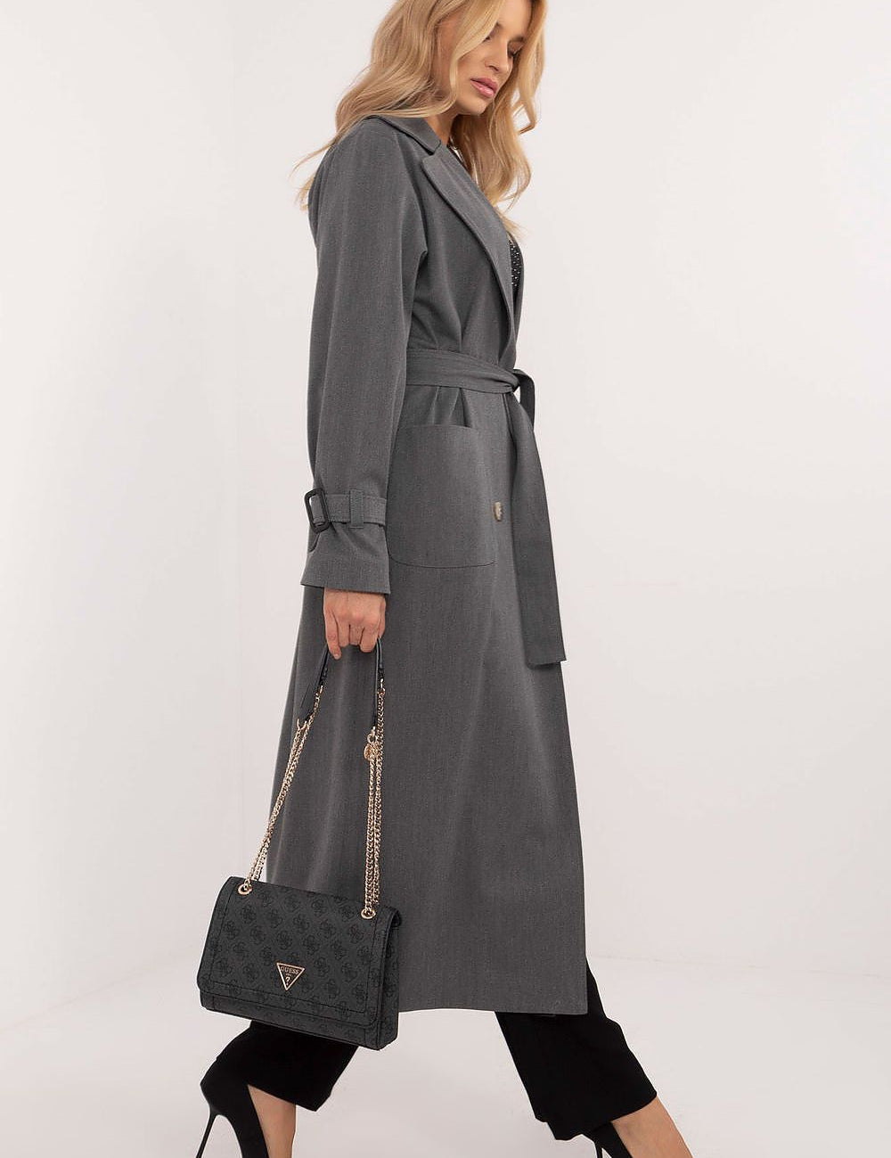 Elegant woman in Elandra double-breasted trench coat, calf-length, classic style, carrying a handbag, wearing black pants and heels.