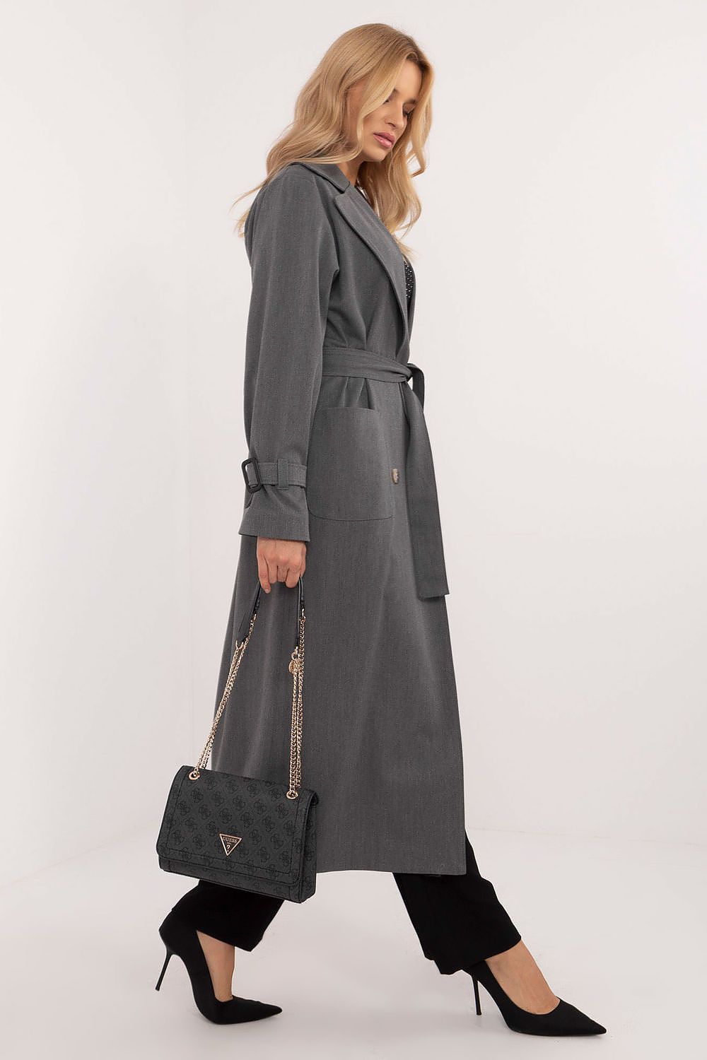 Elegant woman in Elandra double-breasted trench coat, calf-length, classic style, carrying a handbag, wearing black pants and heels.