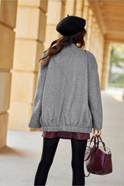 Back view of woman wearing a grey Vernelle stand-collar buttoned jacket with a gathered hem, carrying a purple handbag.