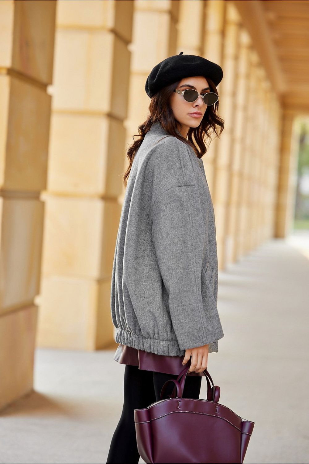 Woman wearing Vernelle Stand-Collar Buttoned Jacket, showcasing dropped shoulder design and gathered hem, with stylish hat and bag.