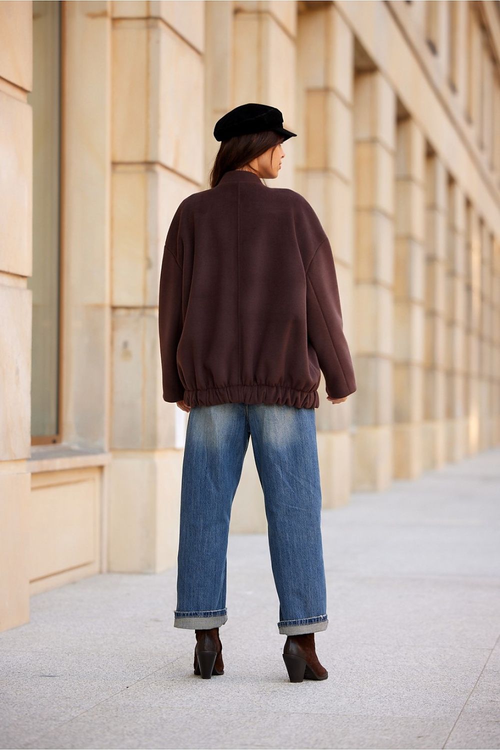 Back view of a woman wearing a Vernelle stand-collar buttoned jacket with dropped shoulders, paired with jeans and a hat.