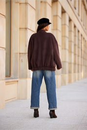 Back view of a woman wearing a Vernelle stand-collar buttoned jacket with dropped shoulders, paired with jeans and a hat.