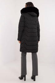 Woman wearing Elvarra quilted down coat with faux fur hood, showcasing knee-length design and durable polyester fabric, side view.