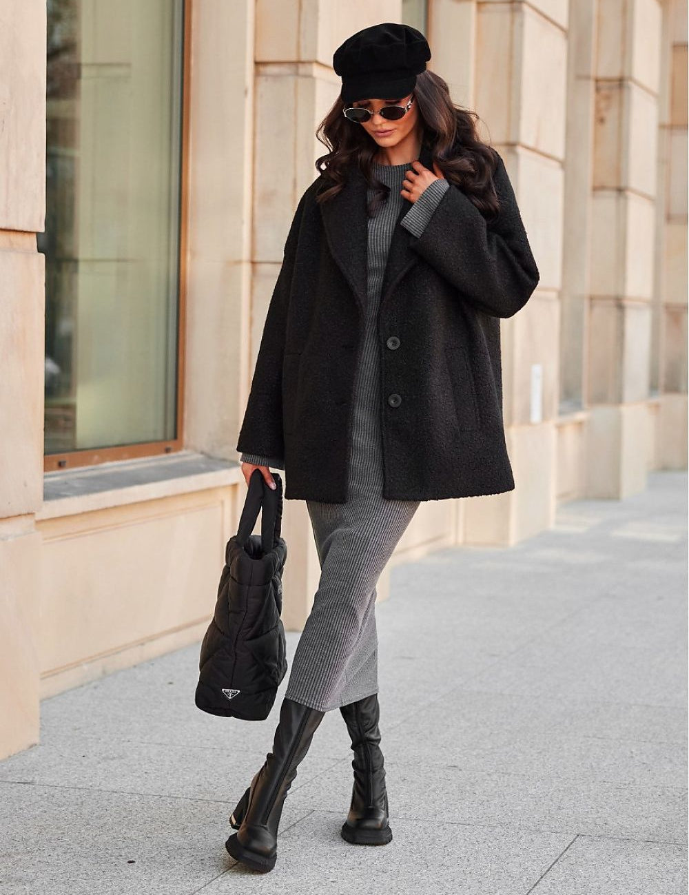 Woman in chic black coat and beret, carrying a stylish handbag while walking confidently on a city street.