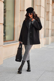 Woman in chic black coat and beret, carrying a stylish handbag while walking confidently on a city street.