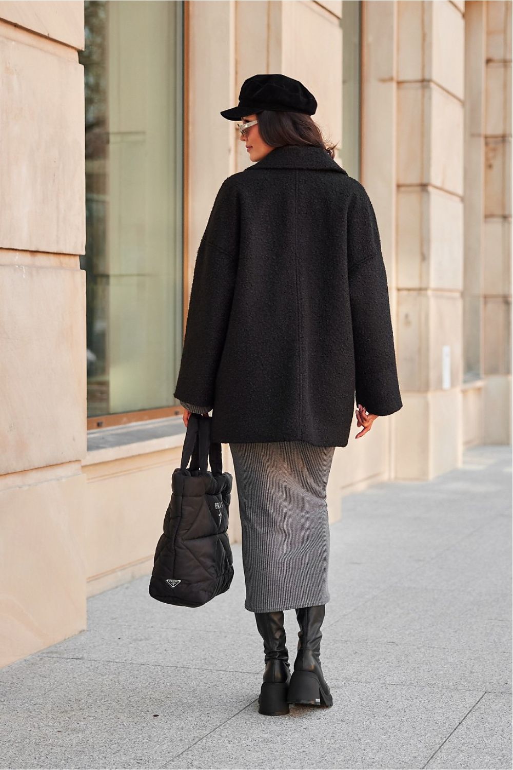 Woman wearing a chic quilted winter jacket and holding a bag, walking on a city street.
