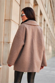 Woman wearing a luxurious tan winter jacket with a relaxed fit and structured collar, walking along a city street.