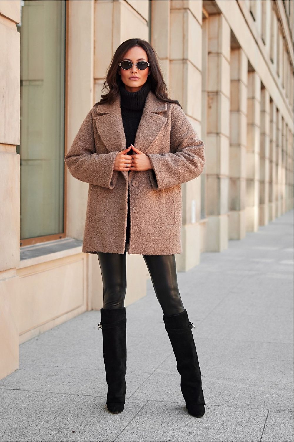 Woman wearing a stylish beige jacket paired with black leggings and tall boots, standing in an urban setting with a confident pose.