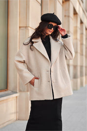 Stylish woman in a beige wool coat and black beret with sunglasses, standing on a city sidewalk.