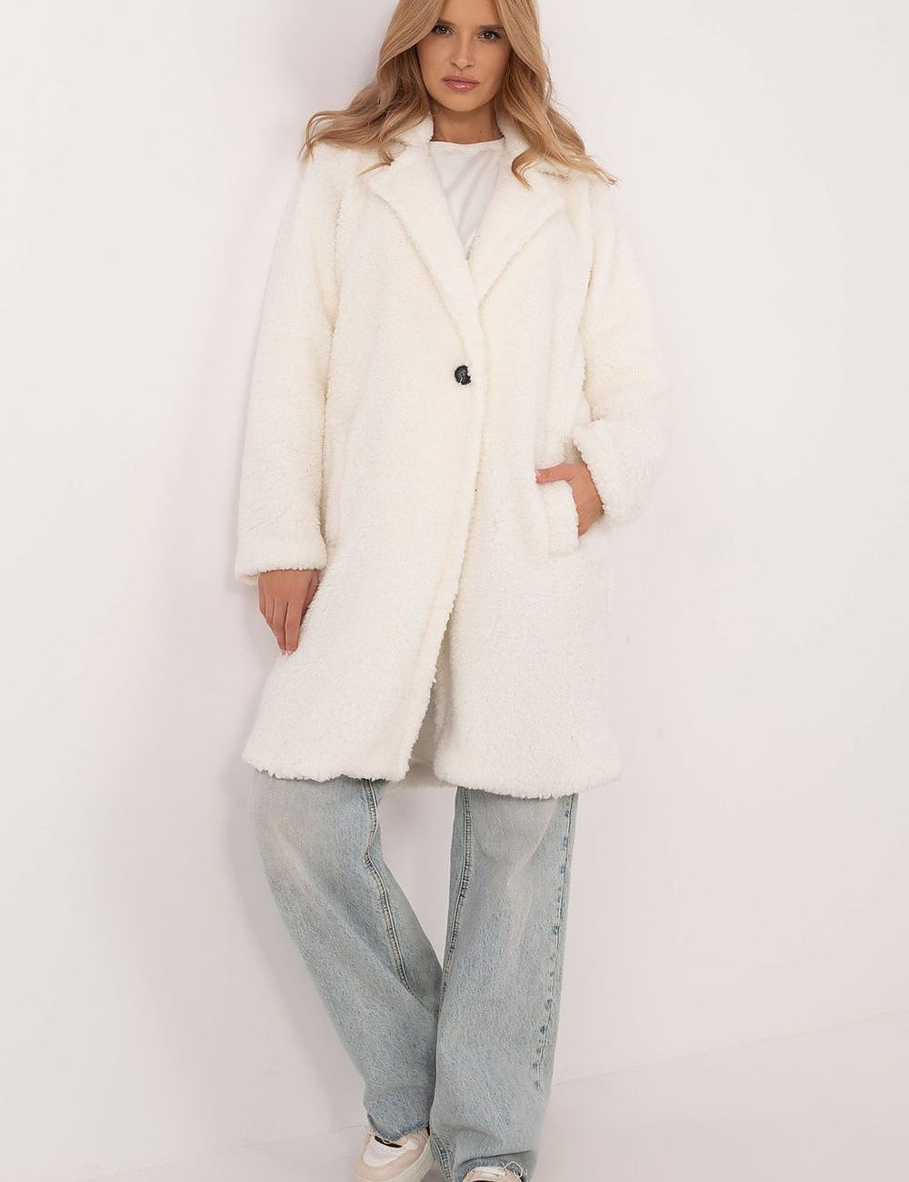 Woman wearing Elantra pre-knee winter coat in white, showcasing elegant design and comfort, paired with jeans and casual shoes.