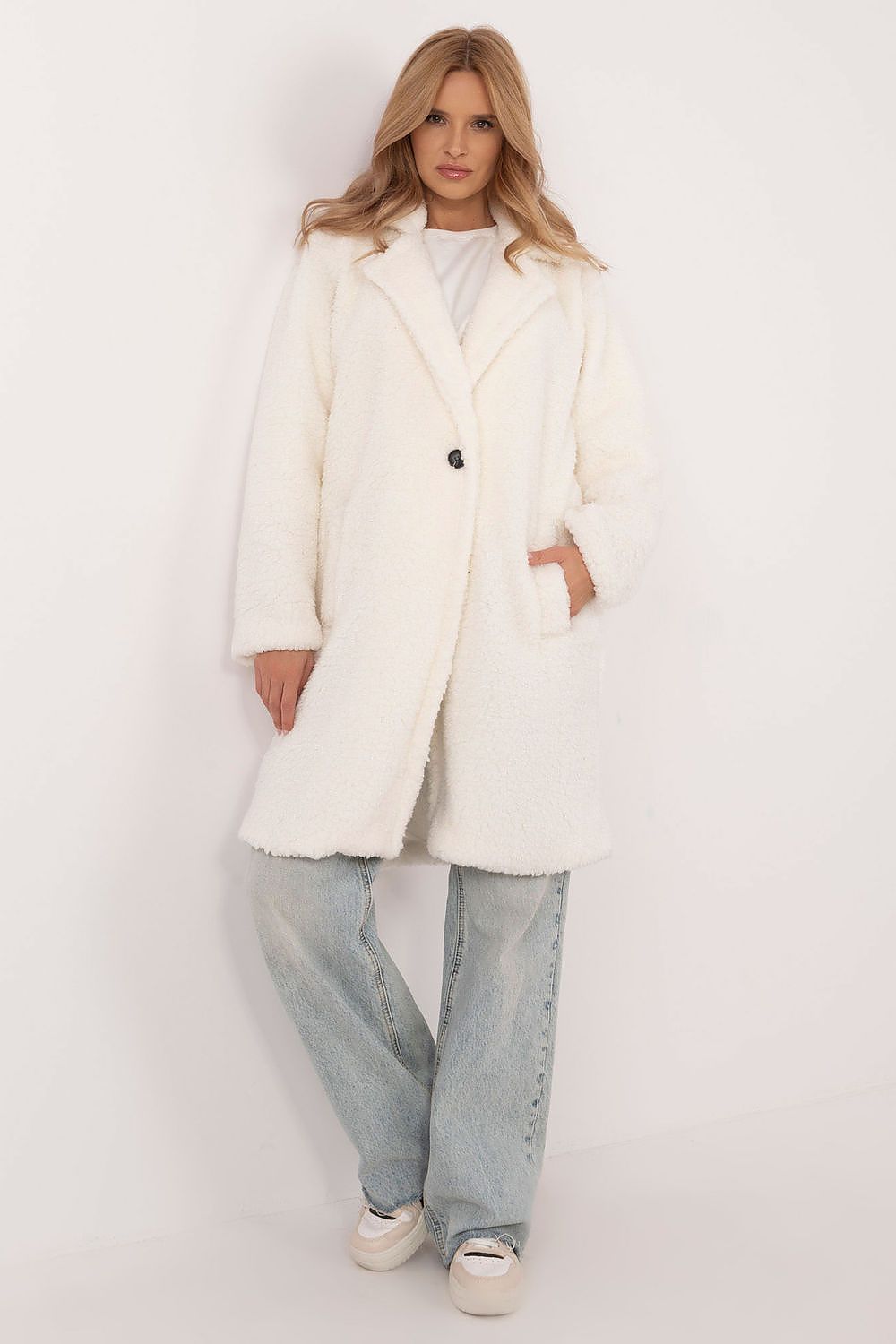 Woman wearing Elantra pre-knee winter coat in white, showcasing elegant design and comfort, paired with jeans and casual shoes.