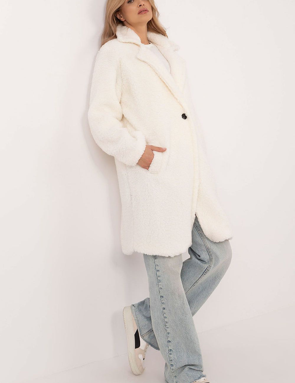 Woman wearing a white Elantra pre-knee winter coat with jeans and sneakers against a plain backdrop, showcasing winter fashion style.