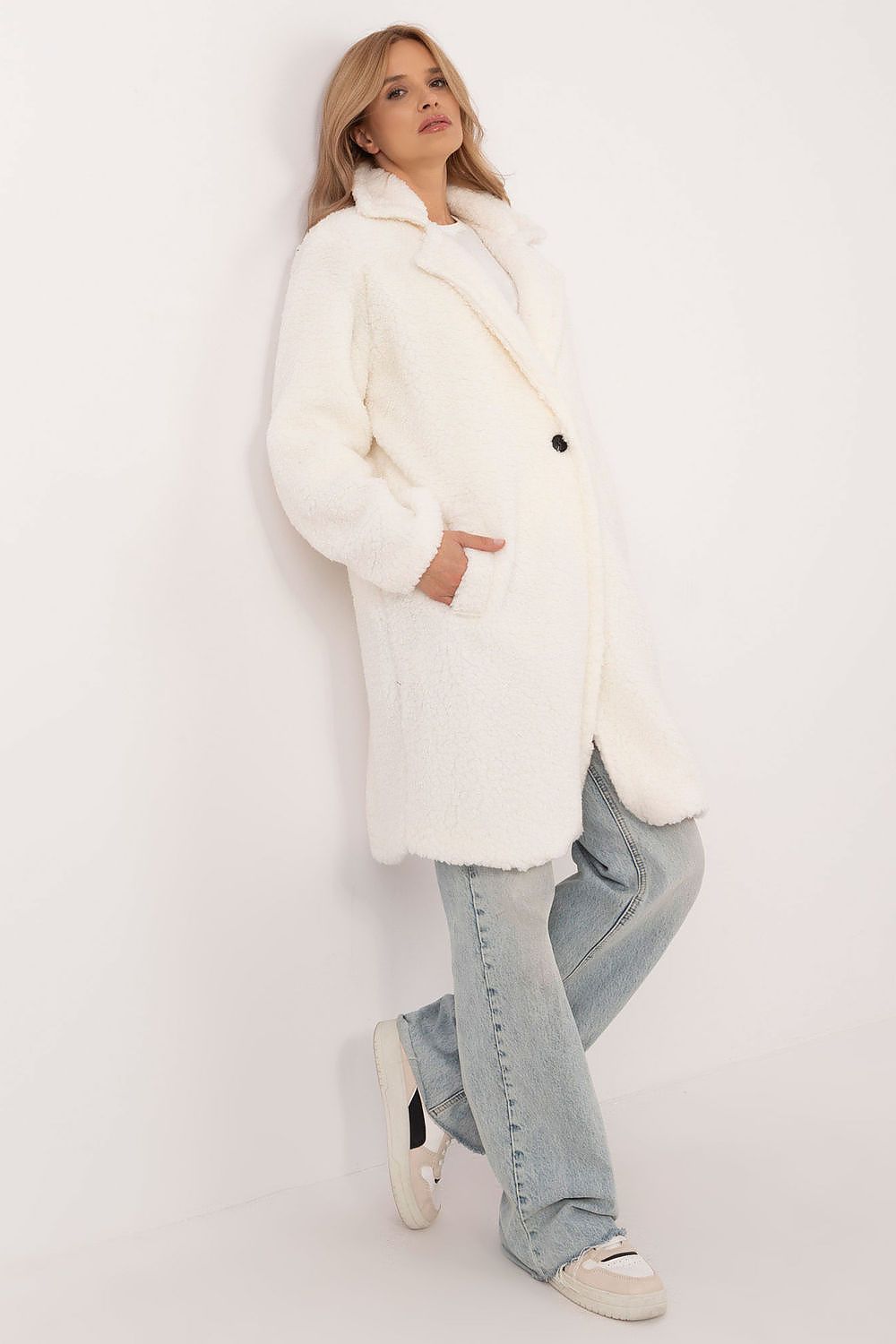 Woman wearing a white Elantra pre-knee winter coat with jeans and sneakers against a plain backdrop, showcasing winter fashion style.
