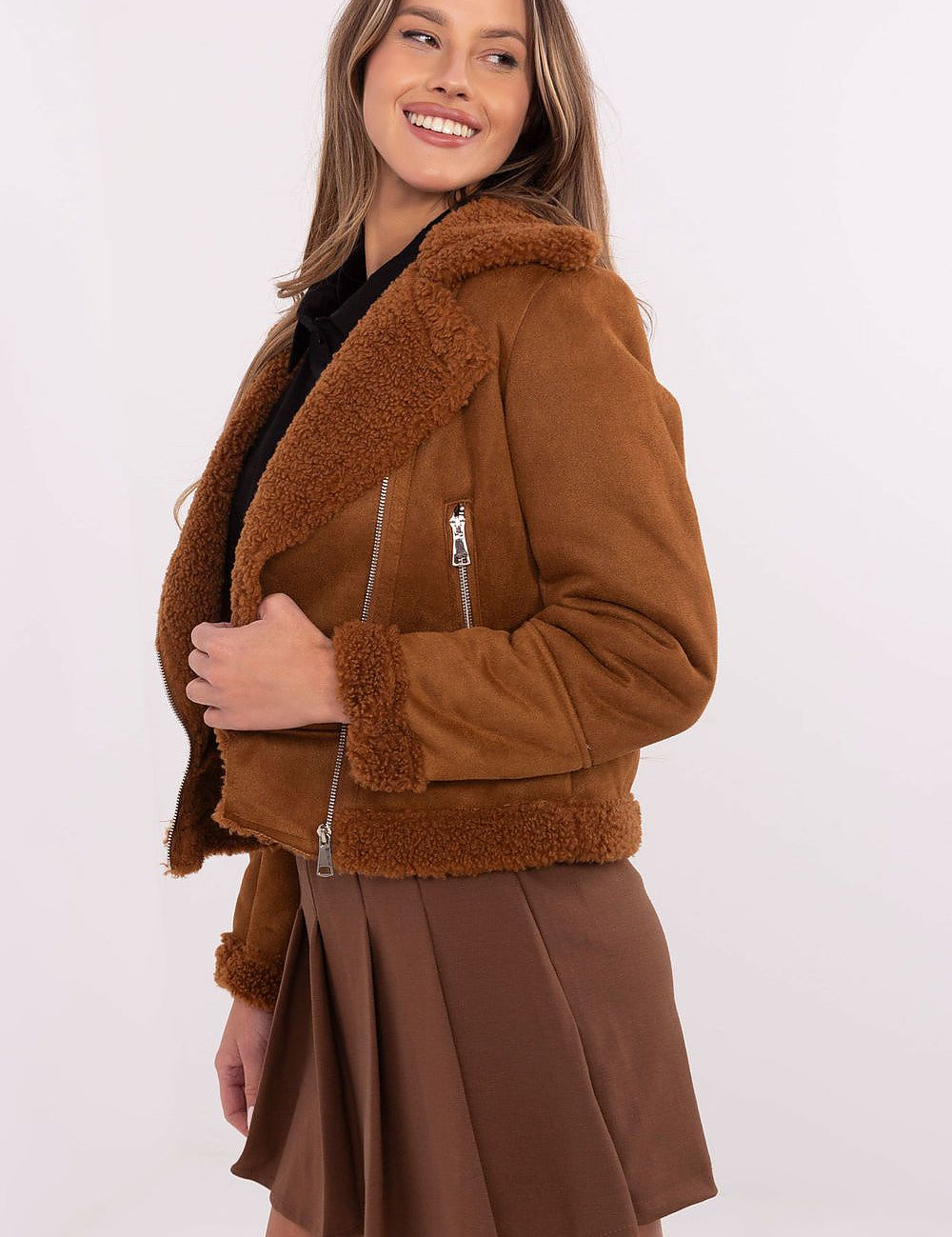 Woman wearing brown shearling jacket with front zipper and shearling collar, paired with brown skirt.