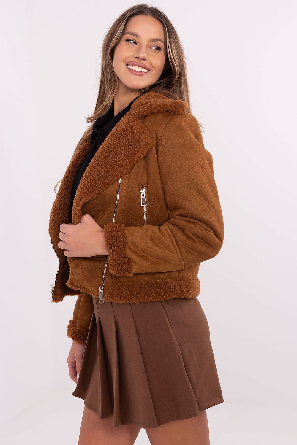 Woman wearing brown shearling jacket with front zipper and shearling collar, paired with brown skirt.