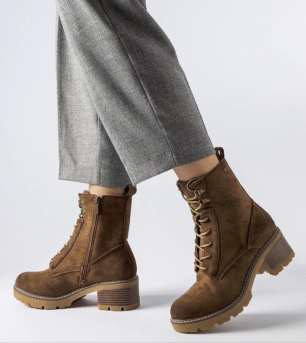 Model wearing Clementina Block-Heel Winter Boots in brown eco leather with side zipper and laces, paired with gray pants.
