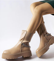 Woman wearing Guglielmo chain-trimmed flat boots with beige sole and gold-tone chain, showcasing modern elegance and comfort.