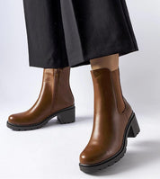 Model wearing Carserra ankle-heel boots in brown eco leather with sleek stiletto heel and zipper closure for elegant style.