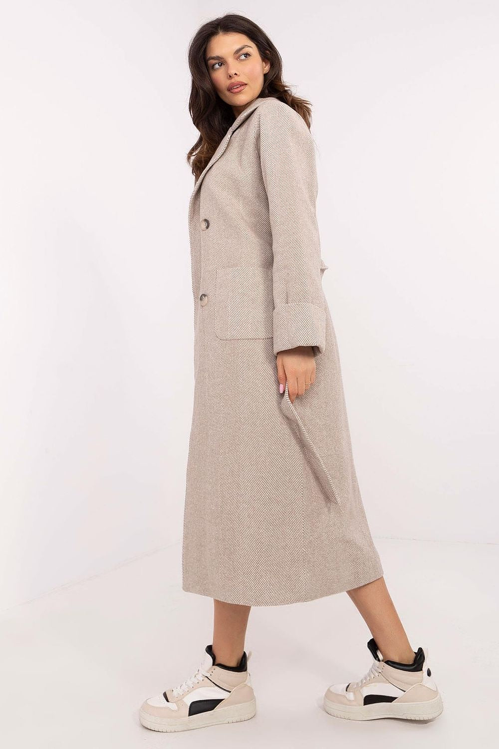 Woman wearing Selvarane long double-breasted wool coat with belted waist and fine stripes, side view, paired with sneakers.