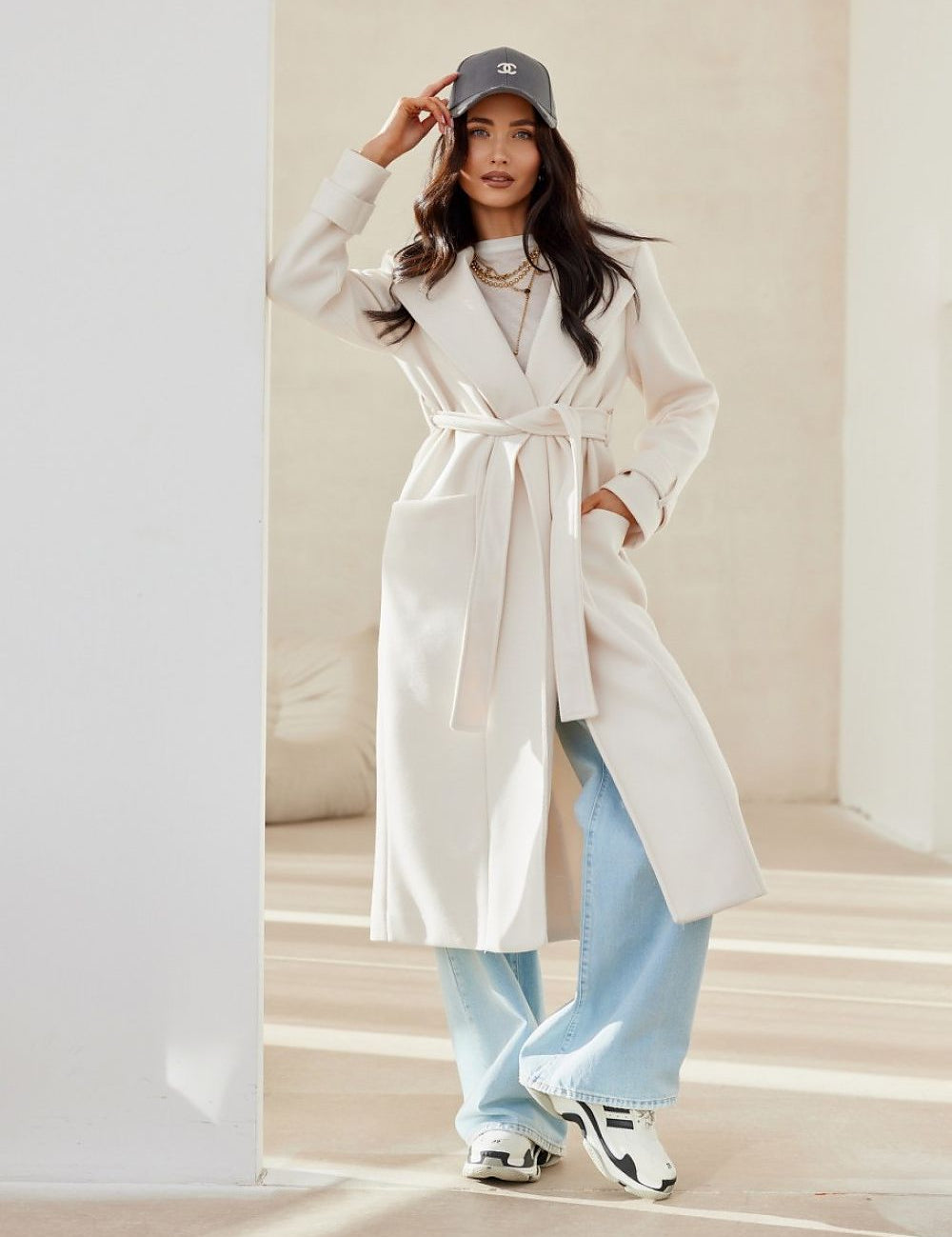 Woman wearing Loravinne Belted Long-Sleeve Lined Coat with classic collar and open pockets, styled casually with blue jeans and a cap.