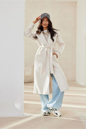 Woman wearing Loravinne Belted Long-Sleeve Lined Coat with classic collar and open pockets, styled casually with blue jeans and a cap.