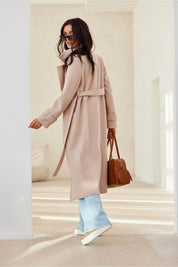 Woman wearing Loravinne Belted Long-Sleeve Coat with brown handbag and sunglasses, showing back view in bright indoor setting.